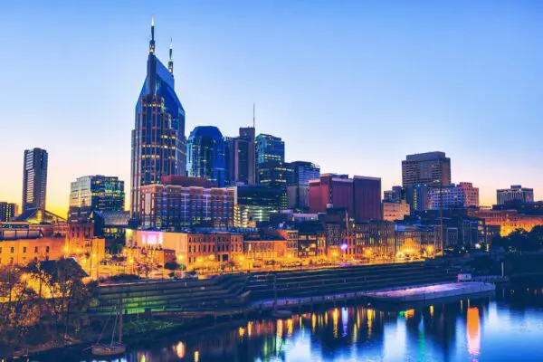 Nashville skyline at dusk with colorful lights reflecting on the river.